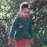 A child walking through leaves in a woodland  and wearing the Little Green Radicals comfy corduroy trousers in ginger.  A corduroy loose fitted trousers in dark orange with a matching drawstring