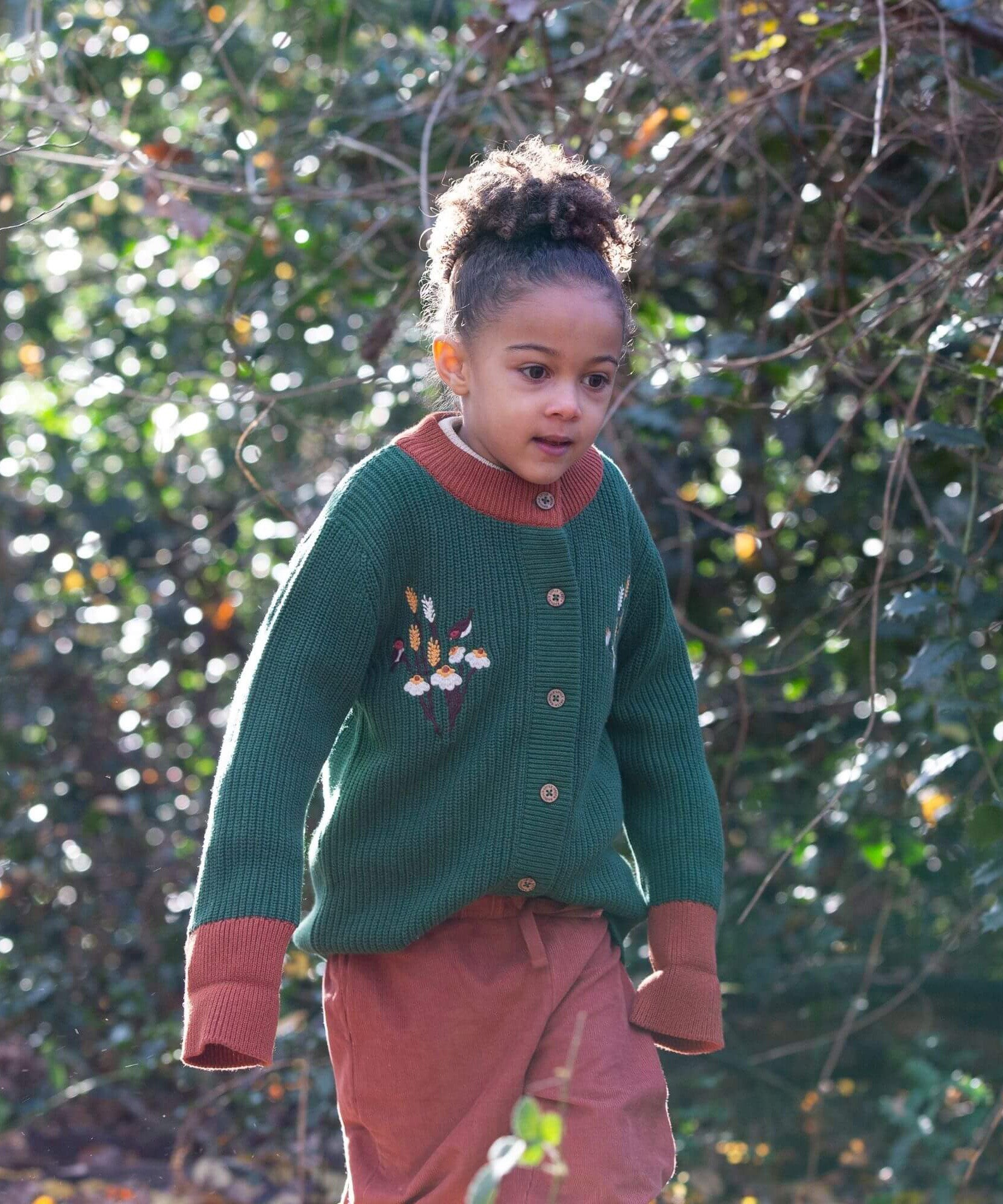 A child walking through leaves in a woodland  and wearing the Little Green Radicals comfy corduroy trousers in ginger.  A corduroy loose fitted trousers in dark orange with a matching drawstring