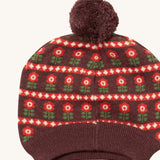 A close up of the Little Green Radicals flower collecting knitted beanie hat showing the retro red flower design detail and brown pom pom on organic cotton fabric.