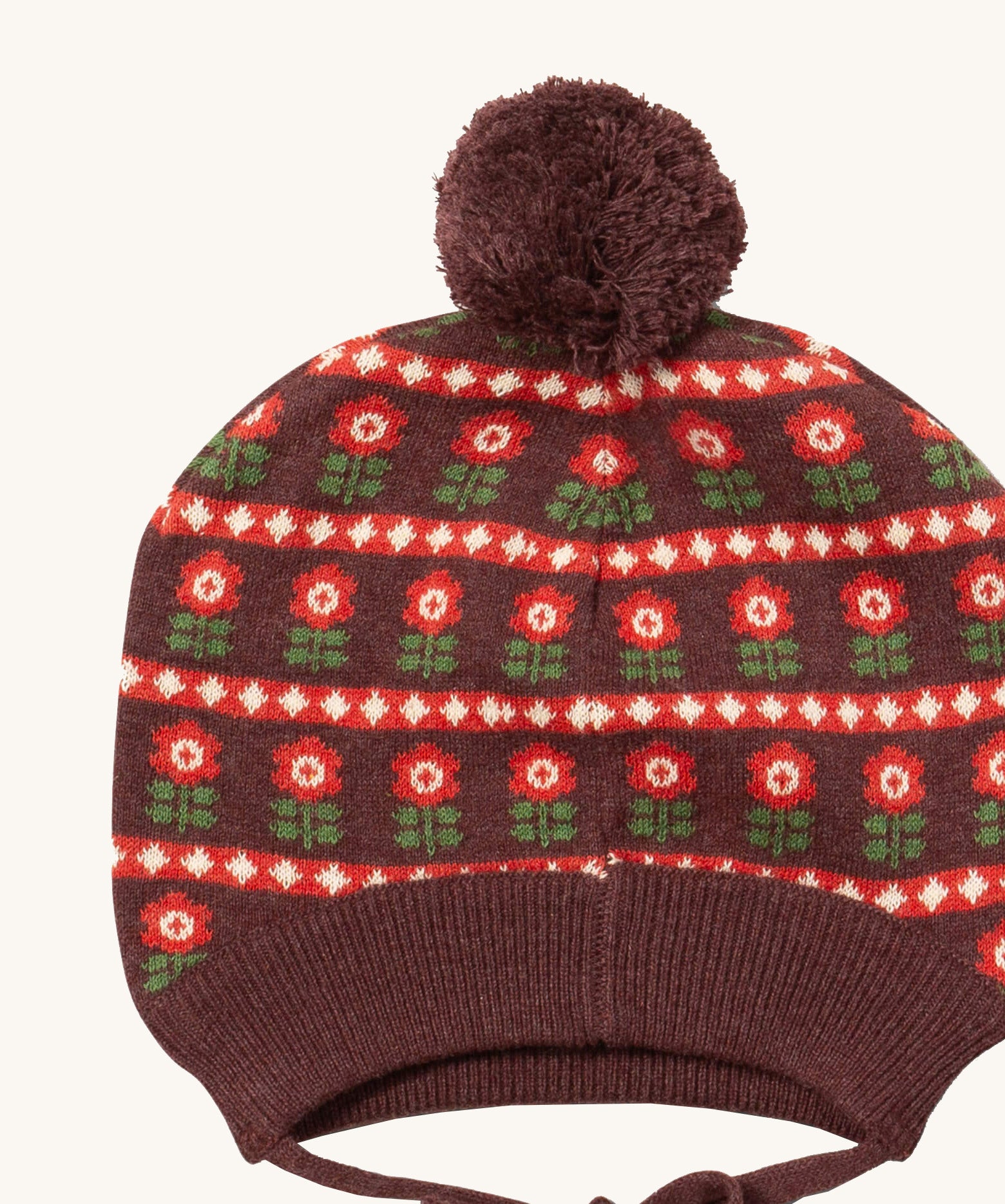 A close up of the Little Green Radicals flower collecting knitted beanie hat showing the retro red flower design detail and brown pom pom on organic cotton fabric.