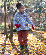 A child walking through leaves in a woodland playing with sticks and wearing the Little Green Radicals comfy corduroy trousers in ginger.  A corduroy loose fitted trousers in dark orange organic cotton fabric