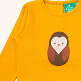 A close up of the Little Green Radicals gold brown owl applique long sleeve top showing the brown owl applique and collar detail on dark yellow organic cotton fabric. 