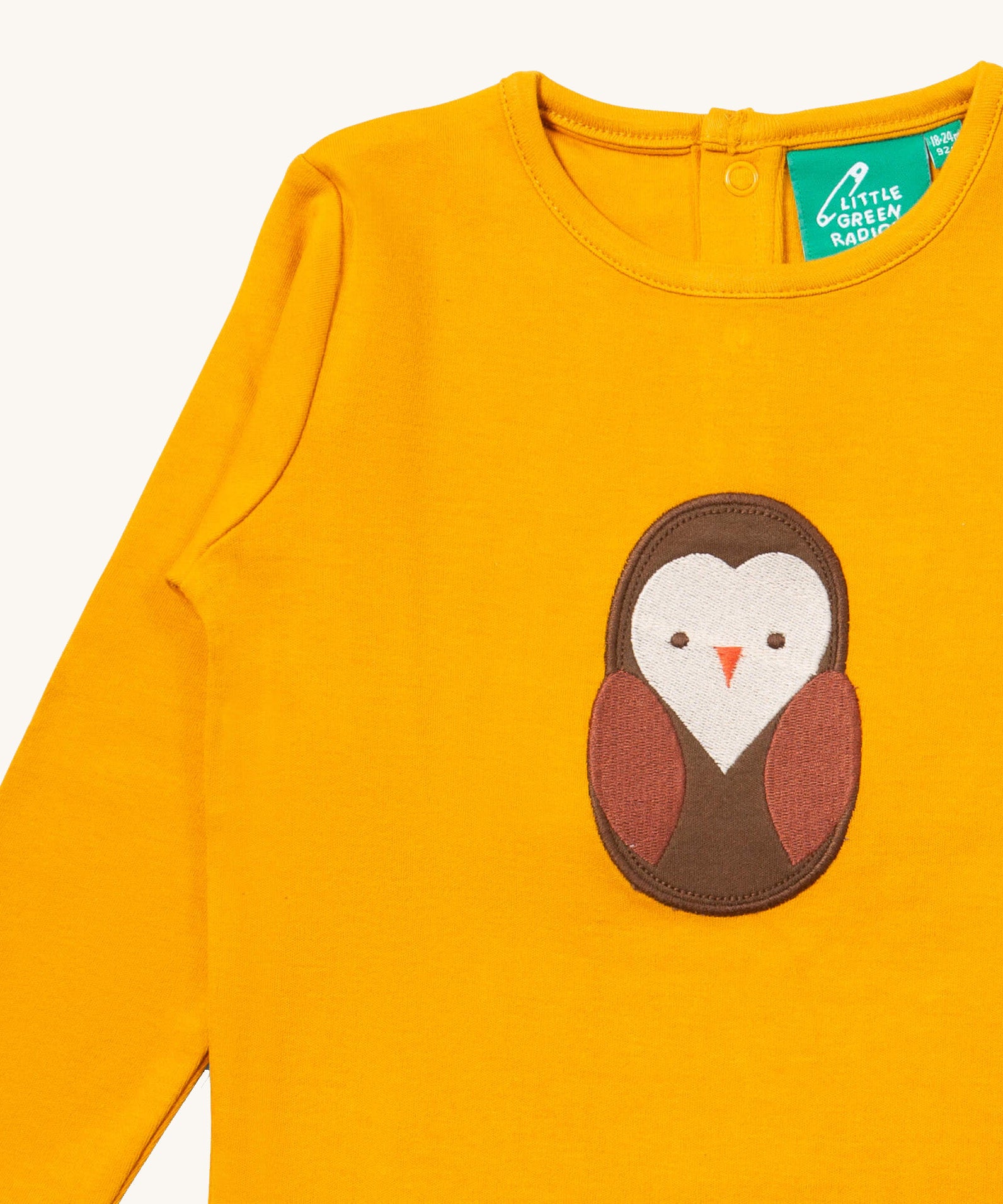 A close up of the Little Green Radicals gold brown owl applique long sleeve top showing the brown owl applique and collar detail on dark yellow organic cotton fabric. 
