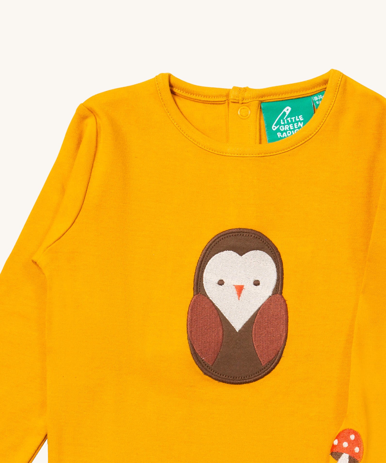 A close up of the Little Green Radicals gold brown owl applique long sleeve top showing the applique and button fastener detail. Features a small mushroom applique on the sleeve on dark yellow organic cotton fabric