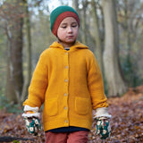 A child standing in woodland wearing the Little Green Radicals gold snuggly hooded knitted cardigan available at Babipur. A thick knitted cardigan with 2 pouch side pockets and button fasteners on yellow organic cotton fabric. 