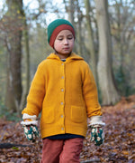 A child standing in woodland wearing the Little Green Radicals gold snuggly hooded knitted cardigan available at Babipur. A thick knitted cardigan with 2 pouch side pockets and button fasteners on yellow organic cotton fabric. 