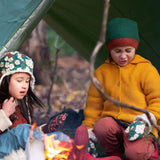 A child outside in woodland wearing the Little Green Radicals gold snuggly hooded knitted cardigan. A knitted cardigan with a generous hood for warmth and button fasteners down the middle on yellow organic cotton fabric. 
