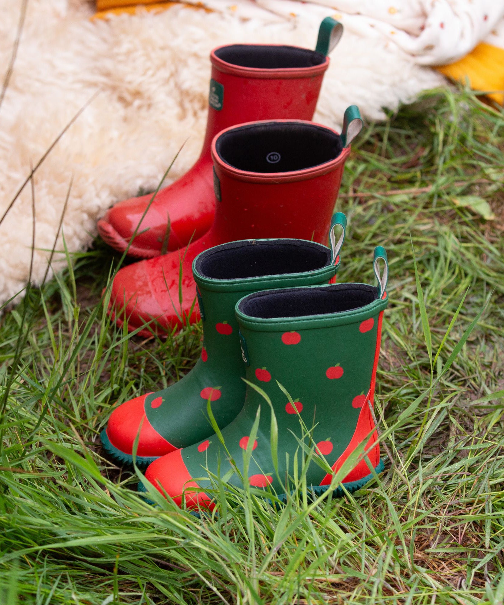 A pair of Little Green Radicals kid wellington boots next to a pair of the red wellies. Natural rubber waterproof wellies. Features a red toe cap, gripped sole and pull-on tab for easy fitting