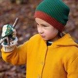 A child in woodland wearing the Little Green Radicals gold snuggly hooded knitted cardigan. A thick knitted cardigan with a generous hood for warmth and button fasteners down the middle with a cream cuff on yellow organic cotton fabric. 