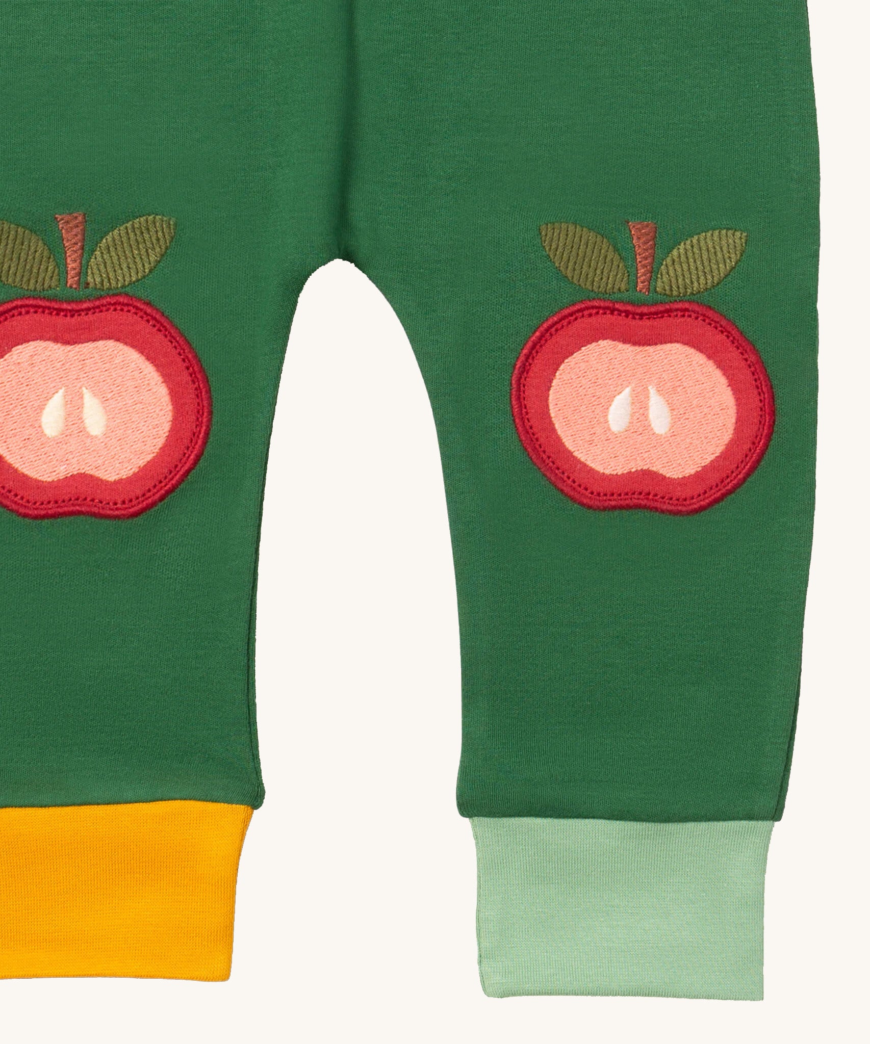A close up of the Little Green Radicals kneepatch joggers in red apples showing the yellow and light green cuff detail organic cotton fabric 