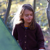 A child wearing the chocolate Little Green Radicals knitted cardigan outside. Showing the button fasteners and the 2 side pouch pockets for storing little treasures.