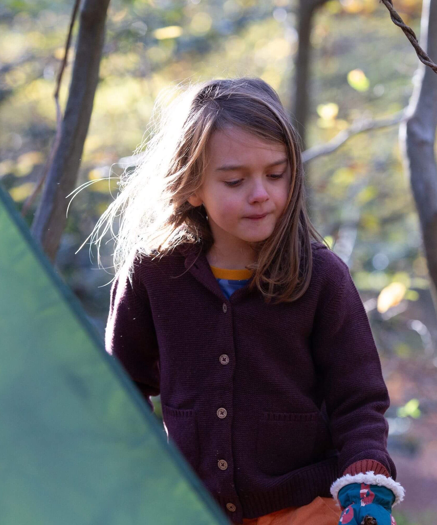 A child wearing the chocolate Little Green Radicals knitted cardigan outside. Showing the button fasteners and the 2 side pouch pockets for storing little treasures.