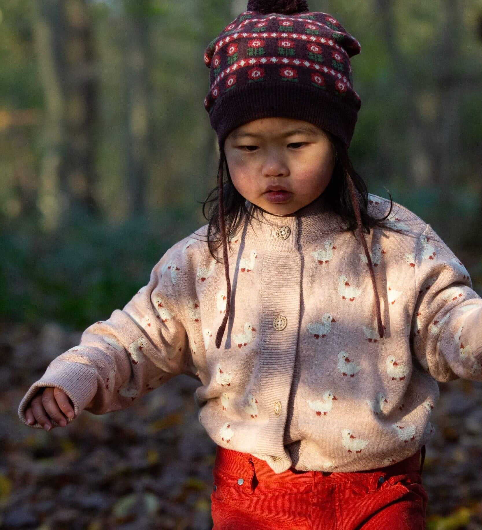 A child wearing the soft pink Little Green Radicals knitted cardigan in puddle ducks outside. Showing the button fasteners and a close up of the white ducks