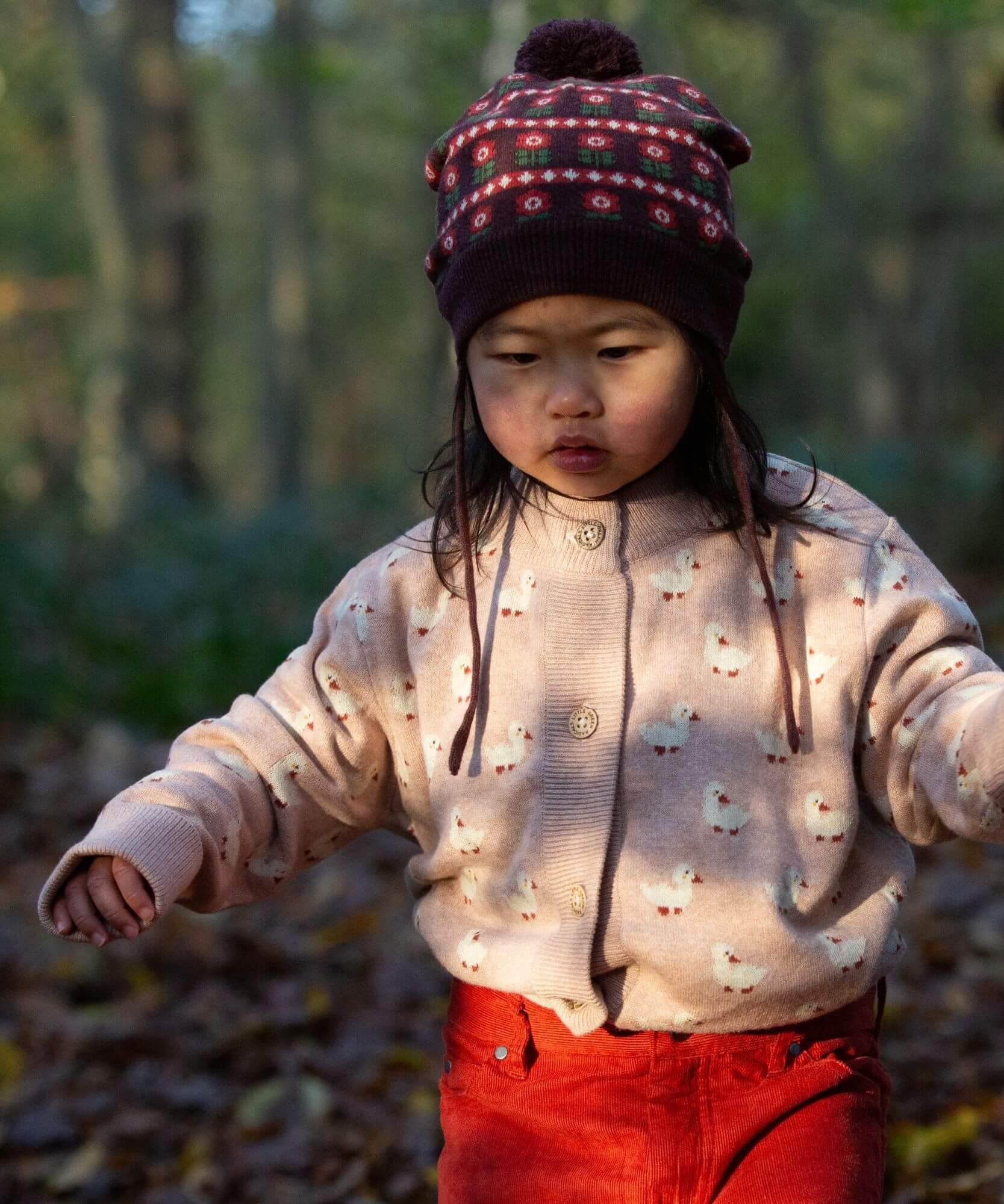 A child wearing the soft pink Little Green Radicals knitted cardigan in puddle ducks outside. Showing the button fasteners and a close up of the white ducks