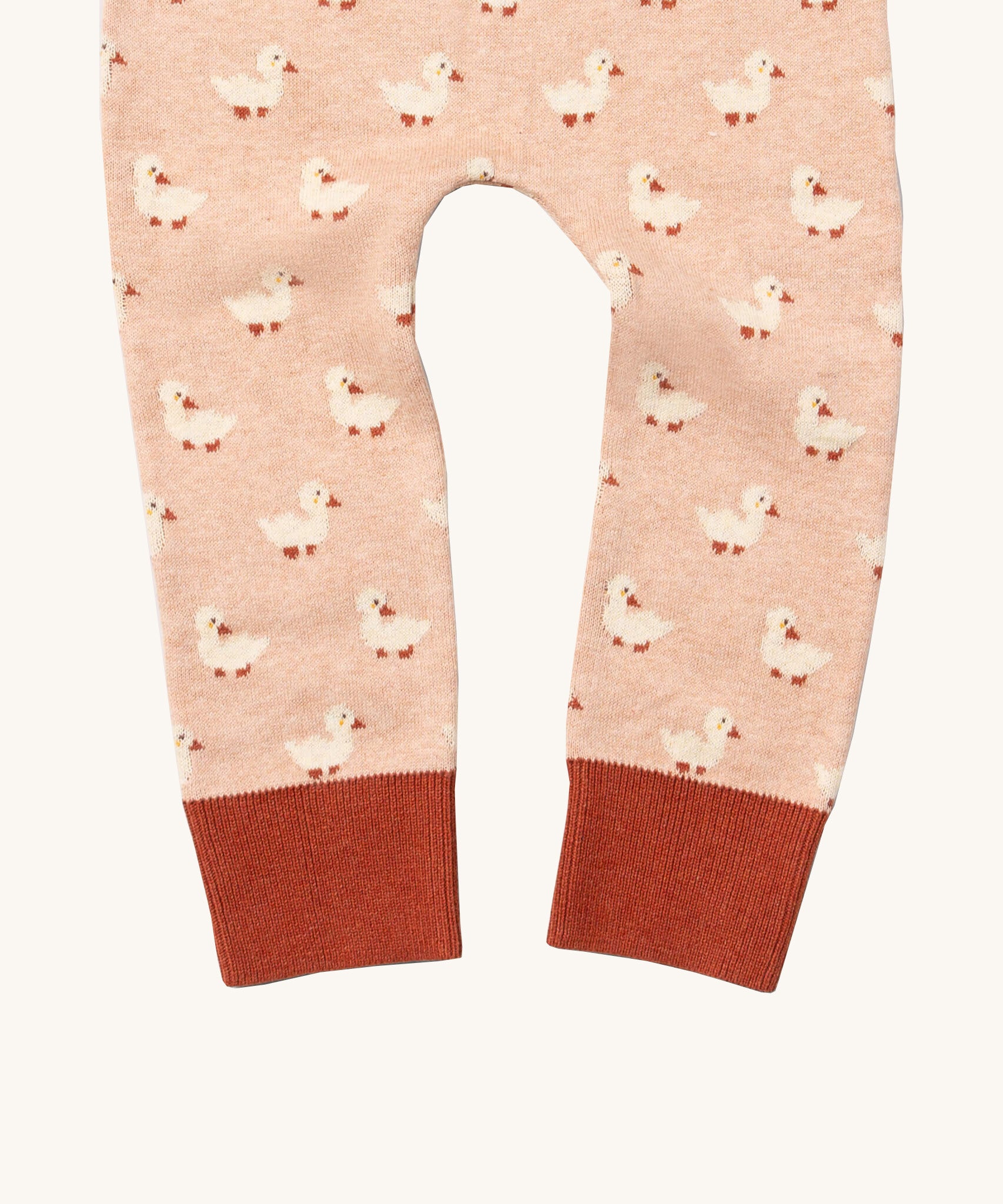 A close up of the Little Green Radicals puddle ducks knitted leggings showing the cute duck detail and red leg cuff on light pink organic cotton fabric