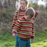 Children wearing the Little Green Radicals knitted snuggly jumper in a  hazel rainbow striped design  with blue corduroy trousers. 