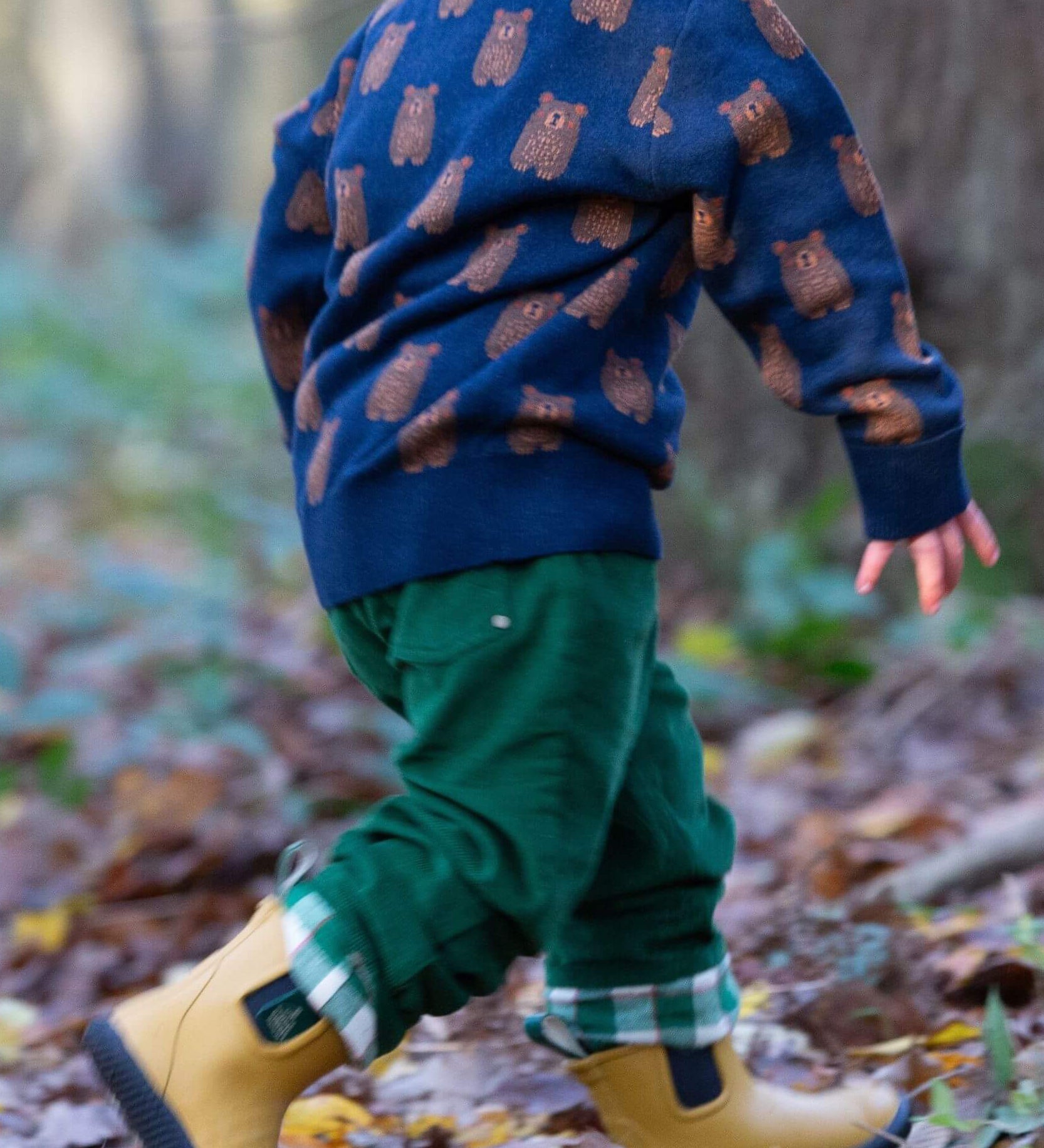 A child running in woodland and wearing the Little Green Radicals navy teddy bears knitted jumper that's available at Babipur. A soft knit jumper with cute brown bears on navy organic cotton fabric.