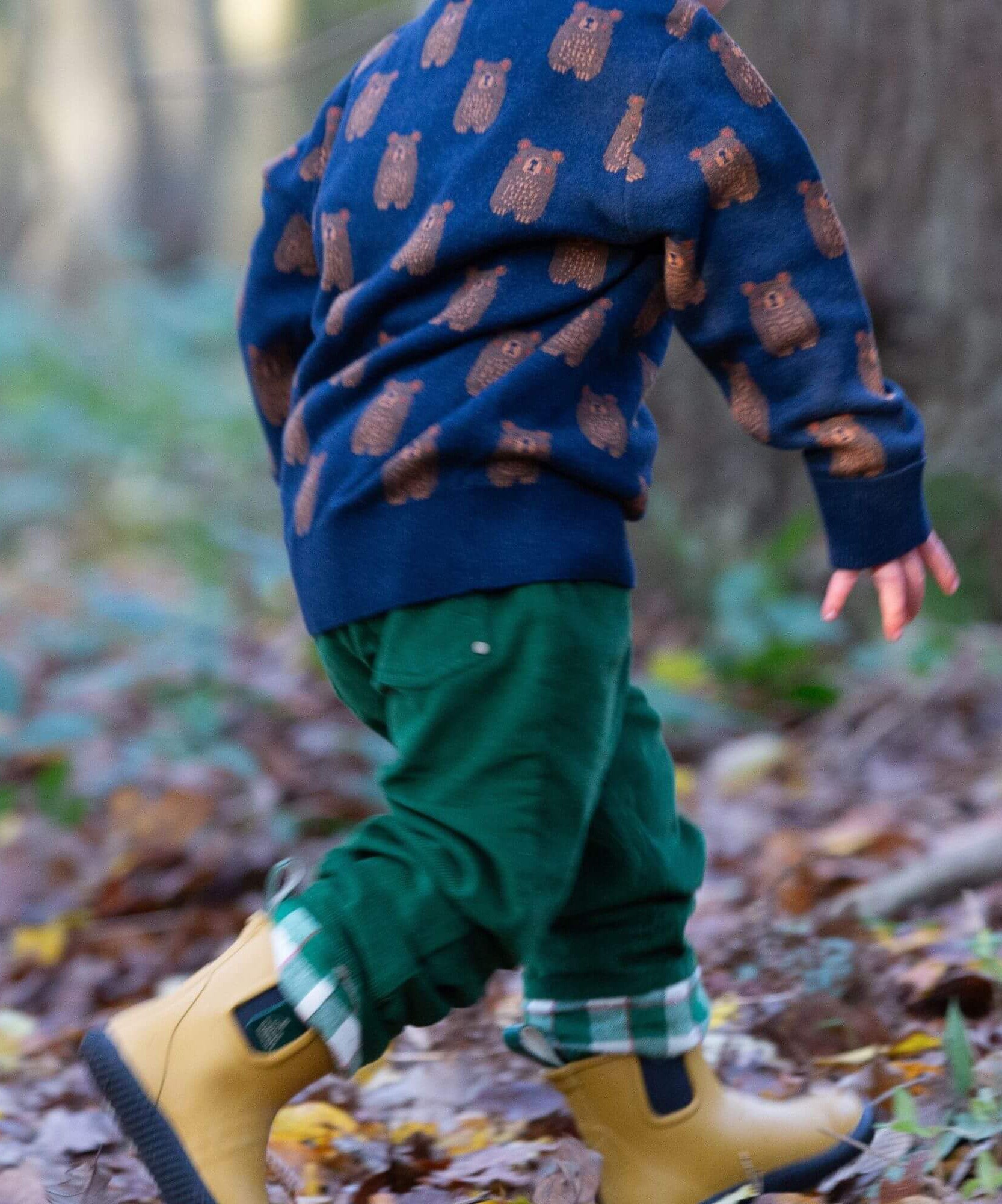 A child running in woodland and wearing the Little Green Radicals navy teddy bears knitted jumper that's available at Babipur. A soft knit jumper with cute brown bears on navy organic cotton fabric.