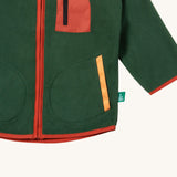A close up of the Little Green Radicals polar fleece jacket in olive showing the chest and pocket detail and a close up of the camp fire appliqué patch on the shoulder. 