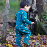 A child walking in the woods and wearing the Little Green radicals turquoise rainbow baby grow. A soft GOTS organic cotton all in one in turquoise with cute rainbow prints