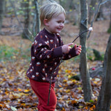 A child in the outdoors wearing the Little Green Radicals brown owl knitted jumper. A soft knit jumper with cute owls and matching thick cuffs and collar for warmth on brown organic cotton fabric. 