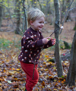 A child in the outdoors wearing the Little Green Radicals brown owl knitted jumper. A soft knit jumper with cute owls and matching thick cuffs and collar for warmth on brown organic cotton fabric. 