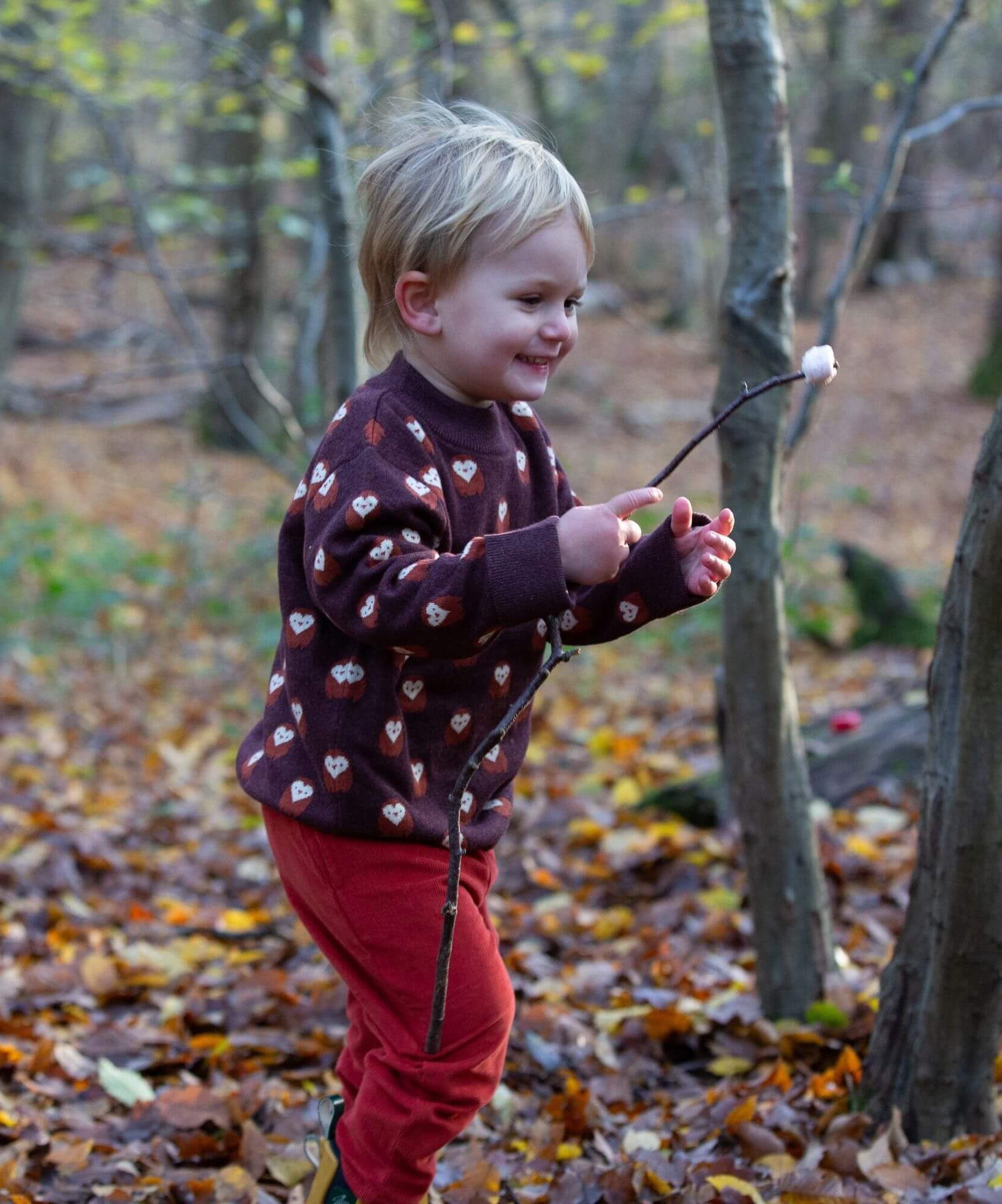 A child in the outdoors wearing the Little Green Radicals brown owl knitted jumper. A soft knit jumper with cute owls and matching thick cuffs and collar for warmth on brown organic cotton fabric. 