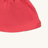 A close up of the Little Green Radicals pink berry waffle tie hat showing waffle knit detail on pink organic cotton fabric