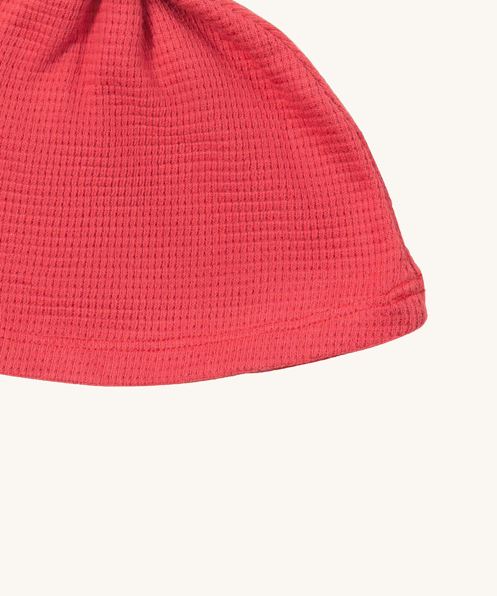 A close up of the Little Green Radicals pink berry waffle tie hat showing waffle knit detail on pink organic cotton fabric
