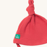 A close up of the Little Green Radicals pink berry waffle tie hat showing the knot detail  on pink organic cotton fabric