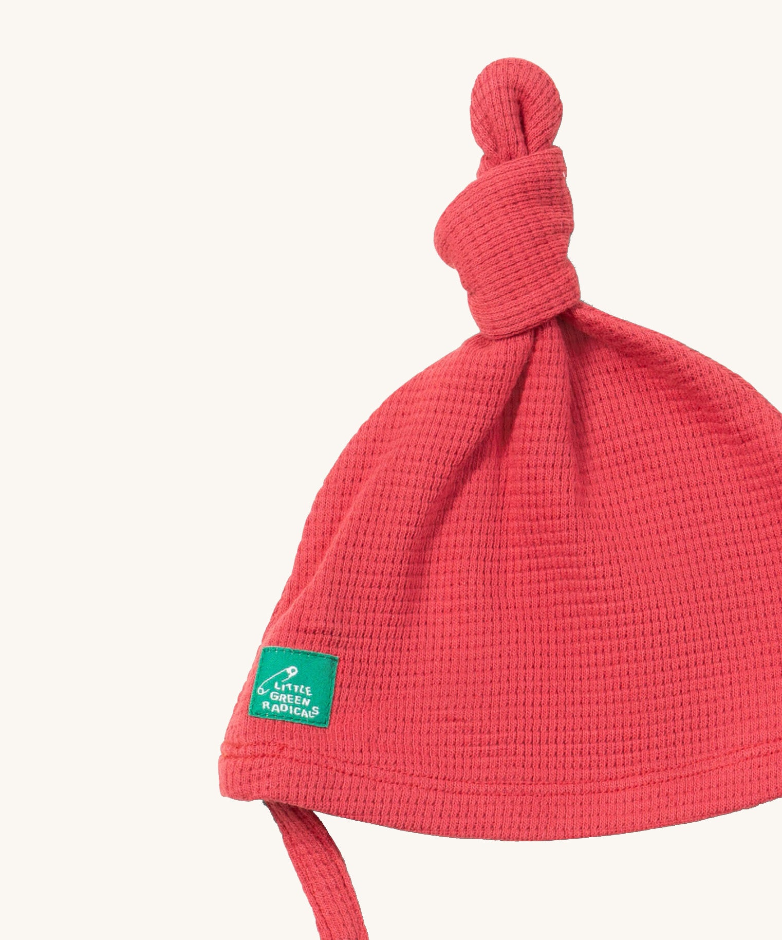 A close up of the Little Green Radicals pink berry waffle tie hat showing the knot detail  on pink organic cotton fabric