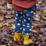 A child standing in  leaves in a woodland wearing the Little Green Radicals comfy joggers in sleeping sheep. A navy jogger with cute prints of sheep on soft GOTS organic cotton fabric