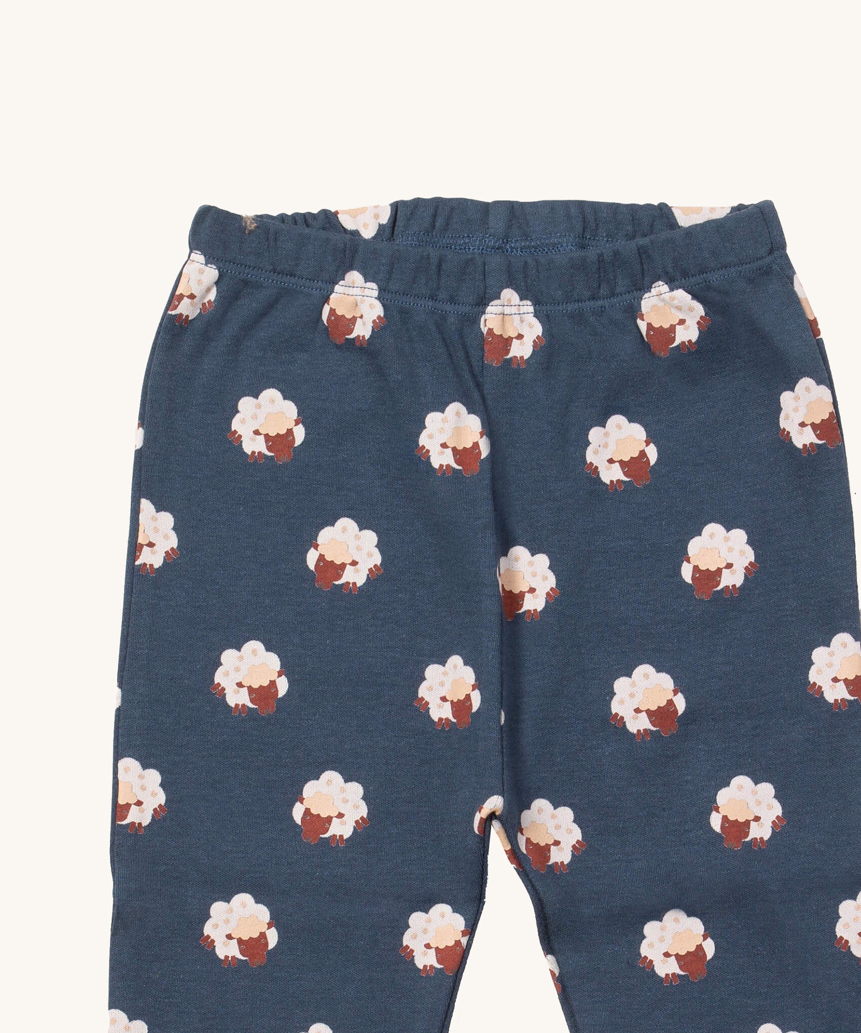 A close up of the Little Green Radicals sleeping sheep pyjama bottom showing the elasticated waist band detail with a close up of the white sheep print detail on navy organic cotton fabric.