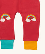A close up of the Little Green Radicals soft red rainbow kneepatch joggers showing the rainbow embroidery kneepatch and the leg cuff detail on pale red organic cotton fabric.