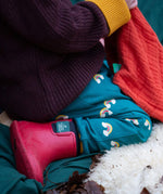 A close up of a child sitting down and wearing the Little Green Radicals turquoise rainbow joggers showing the print detail on organic cotton fabric.