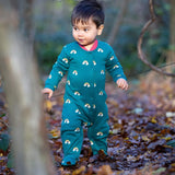 A child walking in the woods and wearing the Little Green radicals turquoise rainbow baby grow. A soft GOTS organic cotton all in one in turquoise with cute rainbow prints. Features popper fasteners on the front and around the crotch 