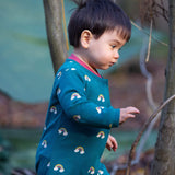 A child walking in the woods and wearing the Little Green radicals turquoise rainbow baby grow. A soft GOTS organic cotton all in one in turquoise with long sleeves and cute rainbow prints 