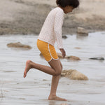 Girl running on sand wearing the LGR yellow swimming shorts and a rose print rash vest