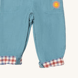 A close up of the Little Green Radicals pale blue lined corduroy dungarees showing the the sun embroidery under the side pocket and the turned up leg cuff showing the check design detail