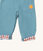 A close up of the Little Green Radicals pale blue lined corduroy dungarees showing the the sun embroidery under the side pocket and the turned up leg cuff showing the check design detail