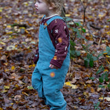 A child walking in the woods and wearing the pale blue Little Green Radicals corduroy dungarees over the quilted flying birds sweater