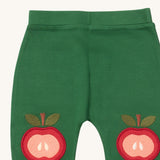 A close up of the Little Green Radicals kneepatch joggers in red apple showing the apple applique detail on green organic cotton fabric