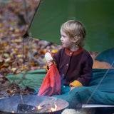 A child sitting outside and wearing the Little Green Radicals knitted cardigan in chocolate available at Babipur. A thick warm brown GOTS organic cotton cardigan with yellow arm cuffs, light brown collar and button fasteners. 