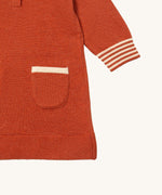 A close up of the Little Green Radicals ginger knitted collar dress. showing the pouch pocket and striped cuff detail on dark orange organic cotton fabric