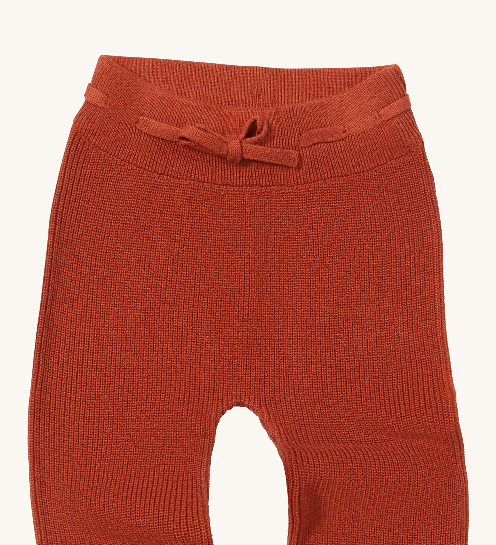A close up of the Little Green Radicals ginger knitted leggings showing the elasticated waist band and drawstring detail on dark orange organic cotton fabric
