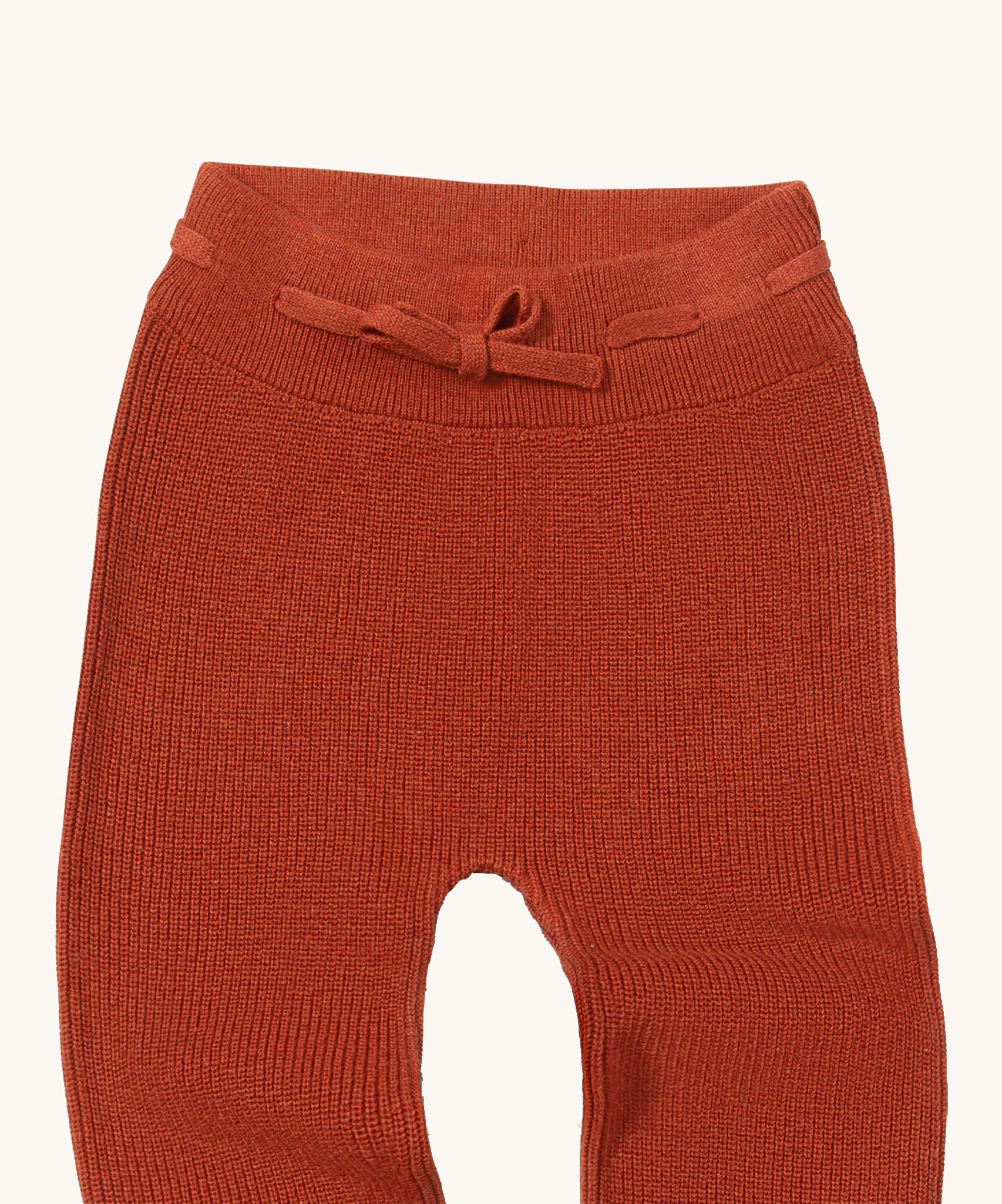 A close up of the Little Green Radicals ginger knitted leggings showing the elasticated waist band and drawstring detail on dark orange organic cotton fabric
