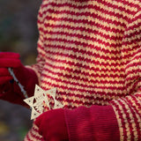 A close up of a child wearing the Little Green Radicals snuggly knitted jumper in juniper stripe. Available at Babipur, this warm knitted jumper comes in pale yellow and red stripes with a matching red arm cuffs that can be turned up.