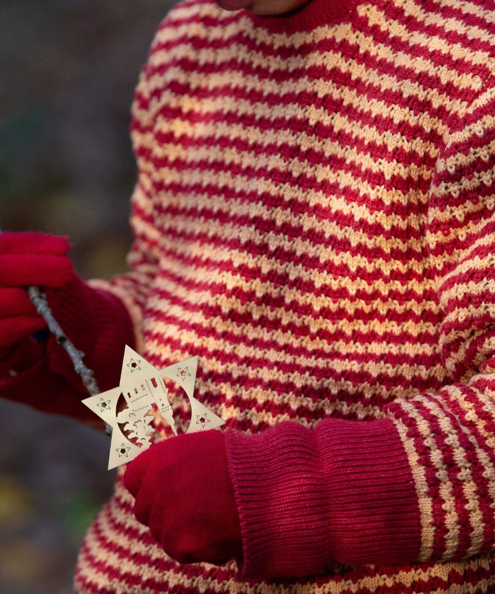 A close up of a child wearing the Little Green Radicals snuggly knitted jumper in juniper stripe. Available at Babipur, this warm knitted jumper comes in pale yellow and red stripes with a matching red arm cuffs that can be turned up.