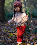 A child wearing the soft pink Little Green Radicals knitted cardigan in puddle ducks outside. Showing the length and fit of the cardigan. 