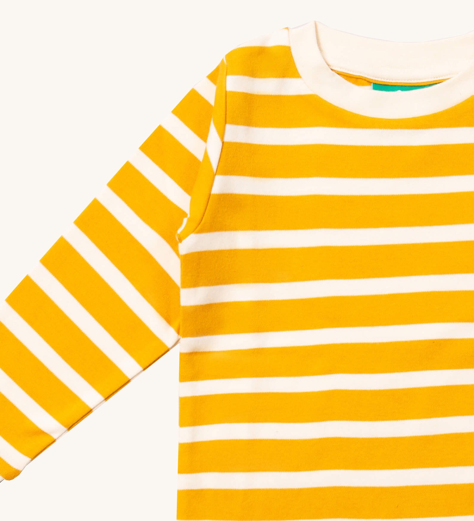 A close up of the Little Green Radicals gold striped long sleeve top that's available at Babipur. Showing the yellow and white stripe detail on organic cotton fabric.